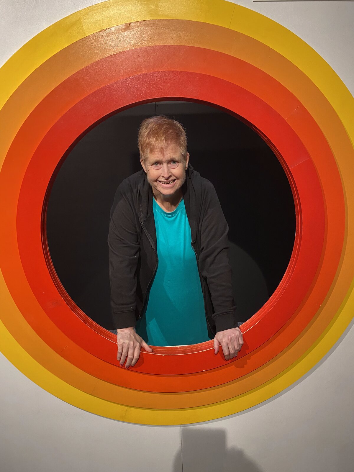 An ATS participant smiling from inside a giant rainbow tunnel slide